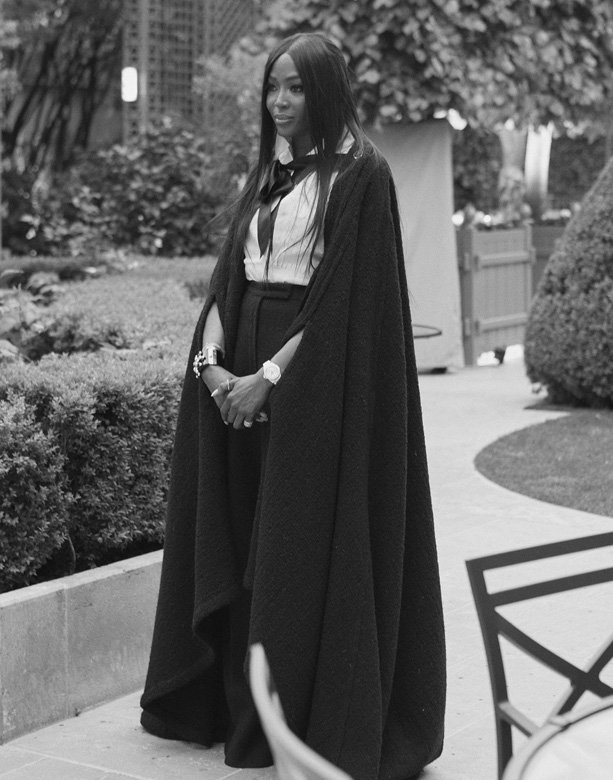 <strong>Naomi Campbell</strong>, English top model and Muse of the new J12 watch, wore a white cotton blouse from the Spring-Summer 2019 Ready-to-Wear collection, with a black fantasy wool tweed cape and black wool cashmere pants, both from the Fall-Winter 2019/20 Ready-to-Wear collection, CHANEL shoes, accessories and makeup, paired with “J12” watch in white ceramic.<br />
 
